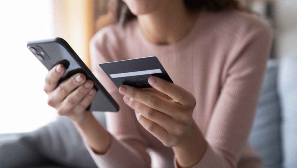 A person holding a credit card in one hand while using their smartphone with the other.
