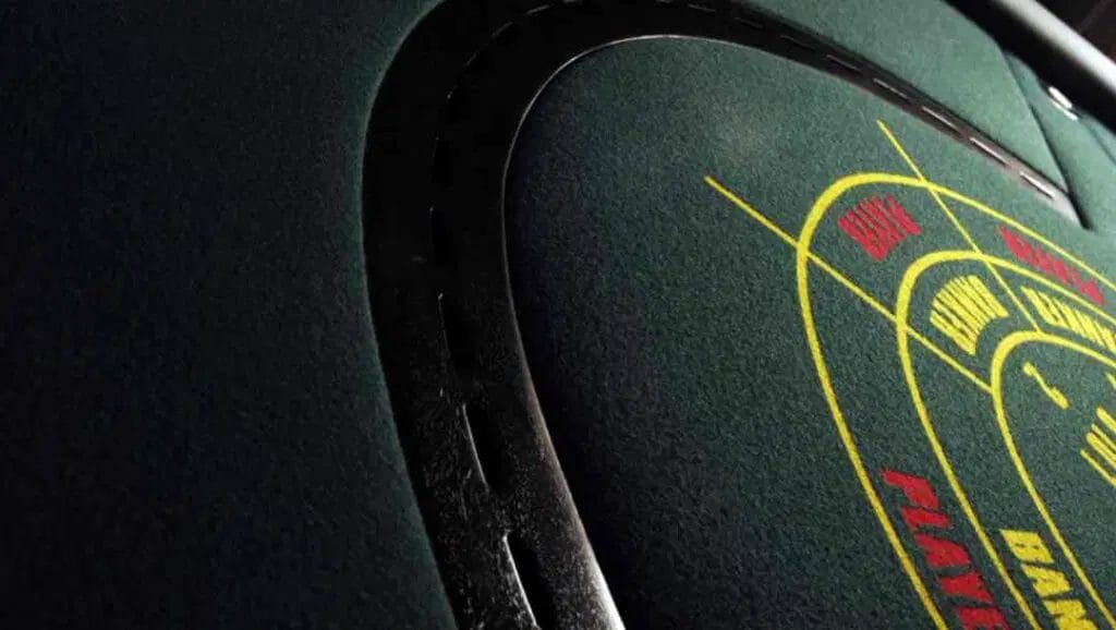 Side-angled close-up of an empty baccarat table with red and yellow writing on green felt.