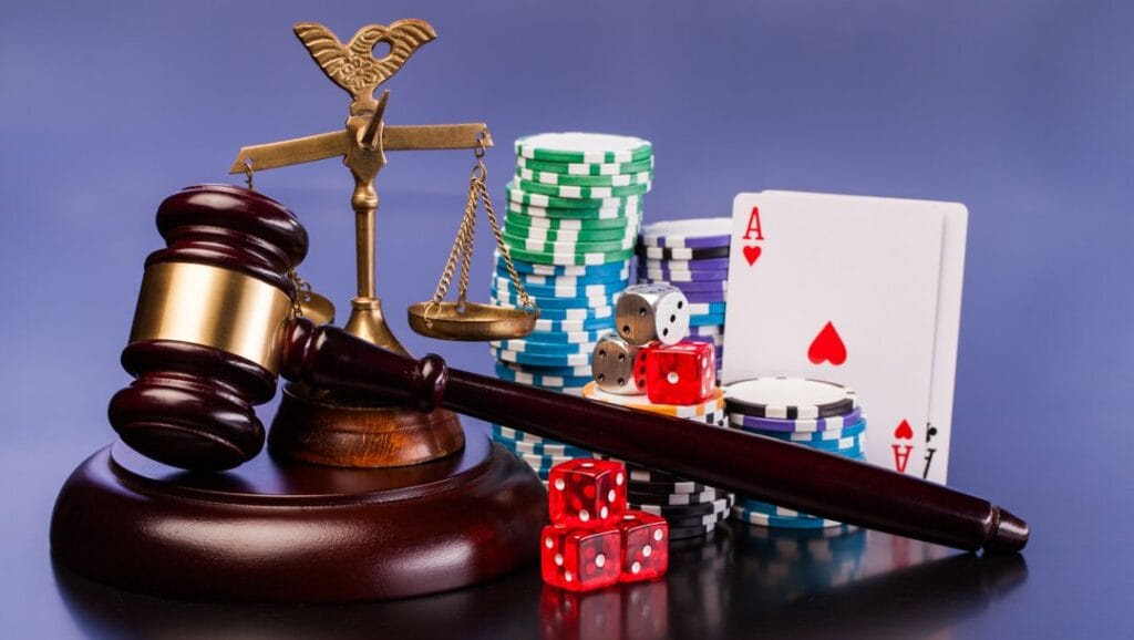 A gavel and scales of justice next to dice, playing cards, and casino chips.