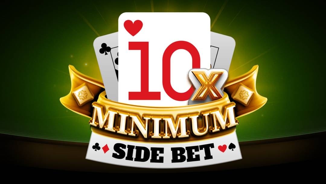 The 10x Minimum Side Bet title screen. The backdrop is the edge of a casino table. The casino table has a green top and wooden edging. In the foreground is the game logo and title. The logo features three layered playing cards. A 10 of hearts is the first of the three cards and it has a gold “x” next to it. Below it is the word “Minimum” in a gold font on a gold ribbon. Below that are the words “Side Bet” between the clubs and diamond symbol on the left and the heart and spade on the right.
